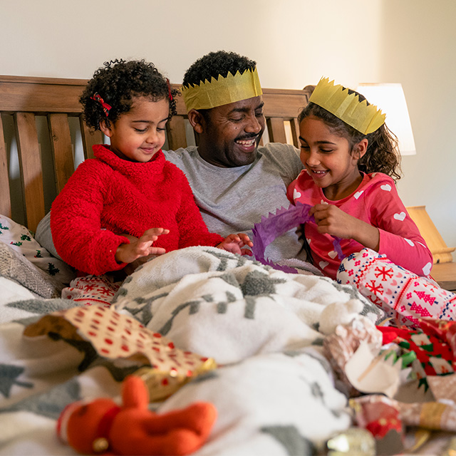 Photo of parent sitting on bed with kids reading a book