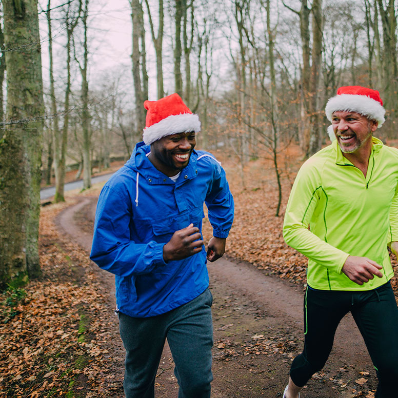 winter homepage festive image 2 men jogging in chilly foggy woods while earing festive red santa hats and rainproof windbreaker jackets