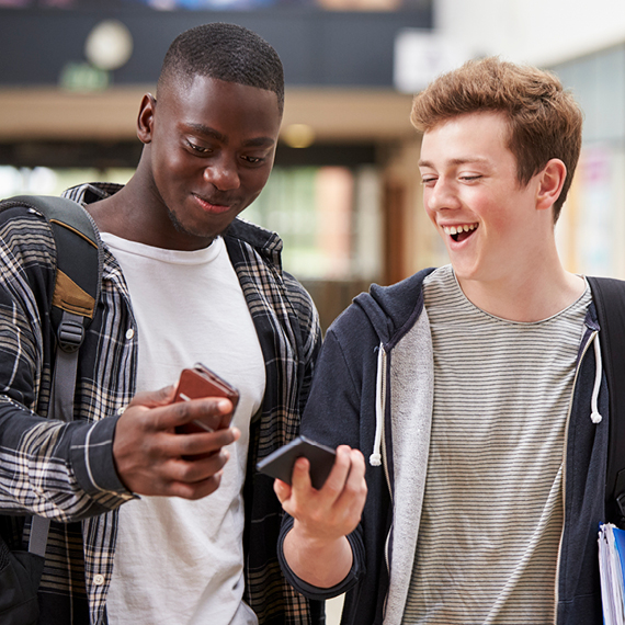 Two young men, looking at a smart phone and smiling.