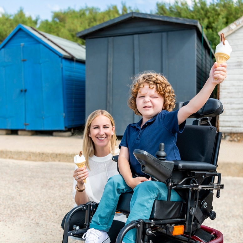 our high summer seasonal image, a picture taken by the beech huts, a straight blonde haired mother - or carer - in a thick collared white short sleeve teeshirt holding a Mr Whippy with flake ice cream, beside her son in wheelchair, also holding a Mr Whippy with Flake, in a black polo, top, trousers and stylish white pumps, with the most wonderful brown curls  