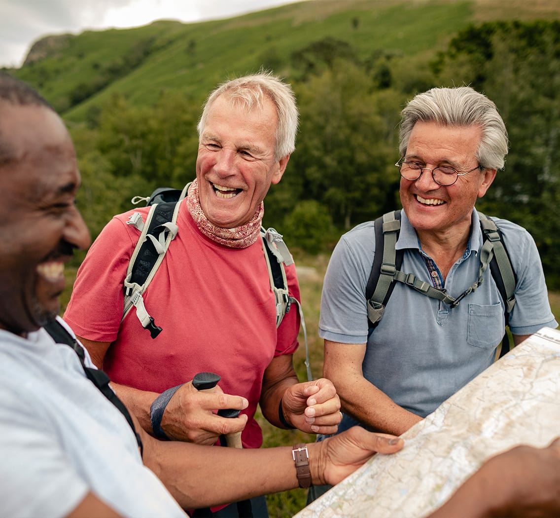 Photo of two men on a hike grinning while a third reads the map