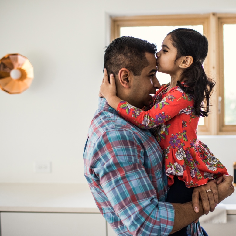 homepage image season late spring father wearing a check shirt holding daughter wearing sundress in his arms so she can kiss his forehead 
