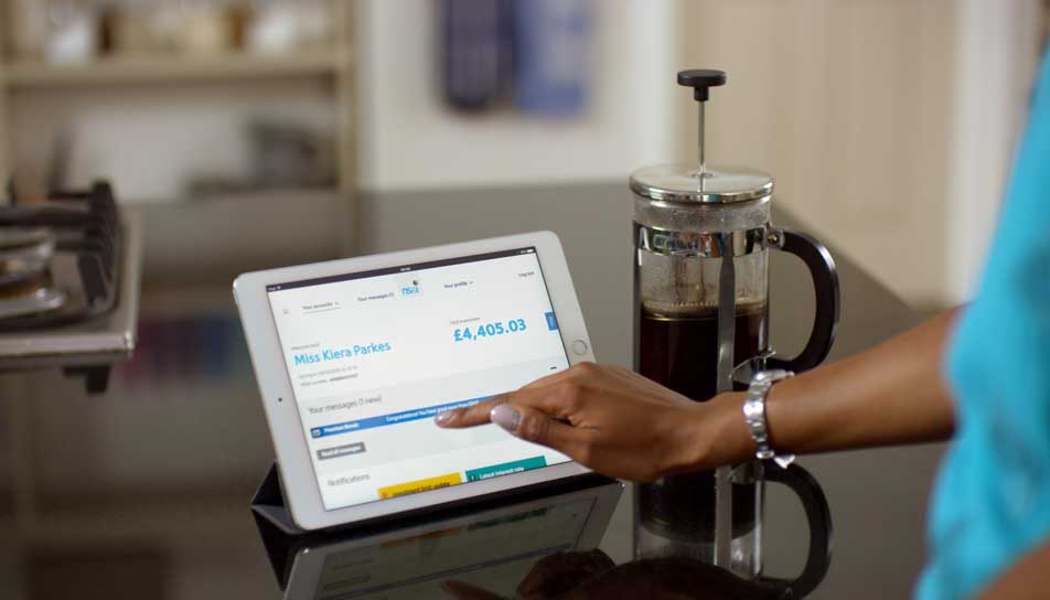 mum using NSANDI transactional site on a tablet next to a cafetiere on kitchen counter